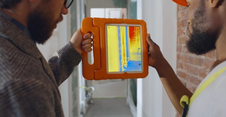 Back view of professional construction team using infrared camera on tablet checking heating system in renovated apartment. Owner and worker with thermal camera inspecting renovation process